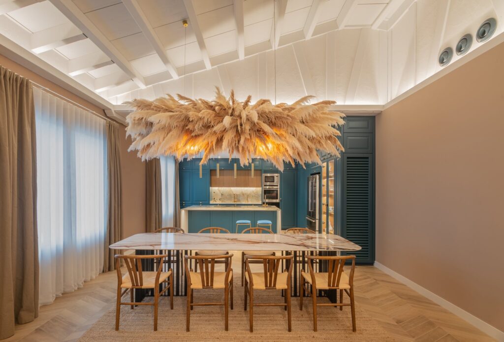 Comedor con lámpara de pampas y cocina azul al fondo