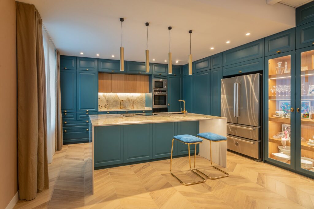 Cocina azul con isla de piedra y vitrinas en roble